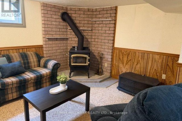 Basement living area with a wood-burning stove, plaid sofa, dark sofa, and coffee table. - Basement - 9 Japonica Road, Toronto