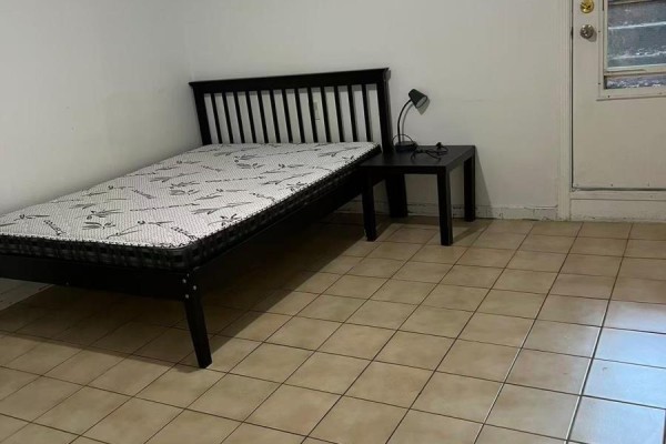 Bedroom with a twin bed, black nightstand with lamp, and door in background. - Basement - 91 Markham Street, Toronto