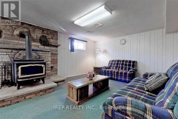 Basement living area with a stone fireplace, wood-burning stove, checkered couches, and coffee table. - Basement - 94 Iangrove Terrace, Toronto