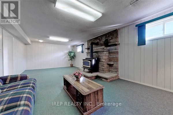 Basement recreation room with white paneled walls, checkered couch, and large stone fireplace. - Basement - 94 Iangrove Terrace, Toronto