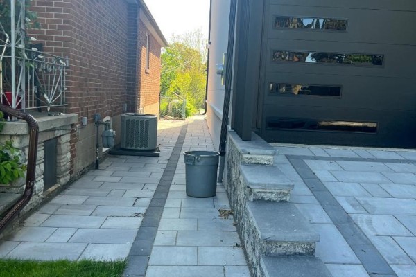 Side walkway between two houses with interlocking pavers, an air conditioning unit, and a garbage can. - Basement Apartment - 50 Brawley Avenue, Toronto