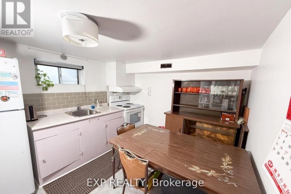 Basement kitchen with a small dining table, stove, and sink, with light cabinetry. - Basement Room 3 - 500 Drewry Avenue, Toronto