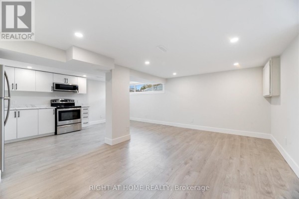 Basement living area and kitchenette with white cabinets, stainless steel appliances, and light wood-look flooring. - Basemnt - 112 Walter Avenue, Newmarket