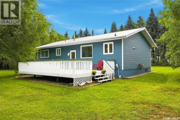 Blue house with white deck and red chairs on grass. - Bellavance Acreage, North Battleford Rm No  437