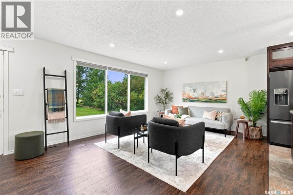 Living room with dark wood floors, white walls, and large window. - Bellavance Acreage, North Battleford Rm No  437