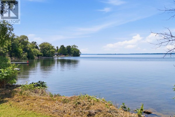 View of a calm blue lake with green shoreline vegetation and trees. - Beside 153 Prinyers Cove Crescent, Prince Edward County
