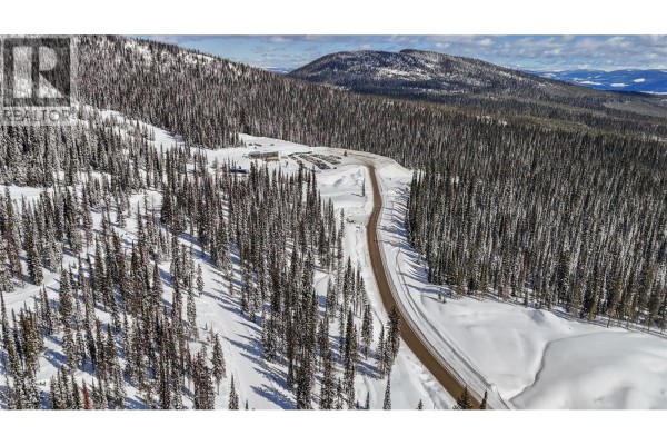 Aerial view of a paved road and parking area in a snow-covered forest with distant hills. - Black Forest Way Lot# 5, Big White
