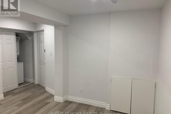 Empty room with white walls, grey wood-look laminate flooring, and doors leading to closets and laundry area. - Bsmet - 75 Maffey Crescent, Richmond Hill