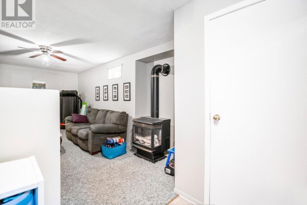 Basement living area with a grey sofa, wood-burning stove, ceiling fan and white door. - Bsmnt - 201 Biscayne Boulevard, Georgina