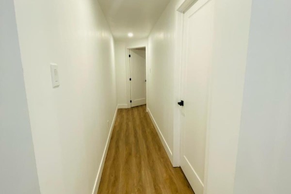 Hallway with white walls, wood-look flooring, and several closed white doors on the right. - Bsmnt - 684 Fenwick Way, Ottawa