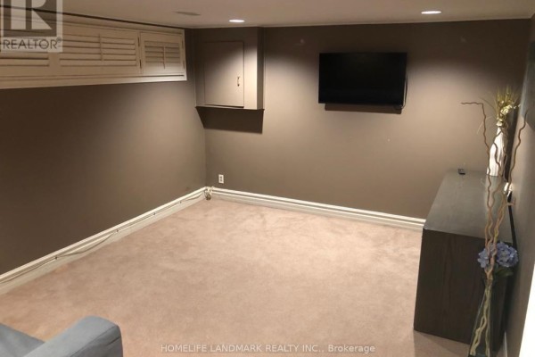 A spacious basement room with beige carpet, grey walls, and a mounted television on the wall. - Bsmt - 10 Oscar Court, Toronto