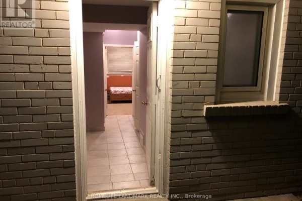View into a basement hallway with beige tile flooring, leading to a bedroom with an orange bed. - Bsmt - 10 Oscar Court, Toronto