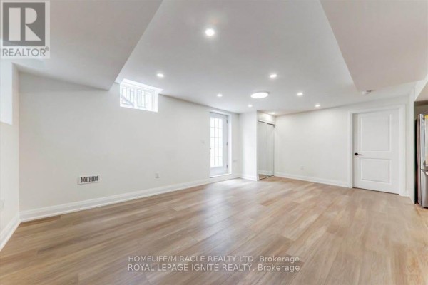 Spacious basement living area with light wood laminate flooring, recessed lighting, and a walk-out door. - Bsmt - 1006 Pelican Trail, Pickering