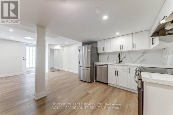 Open-concept basement with kitchen area and living space, featuring white cabinets and light wood flooring. - Bsmt - 1006 Pelican Trail, Pickering