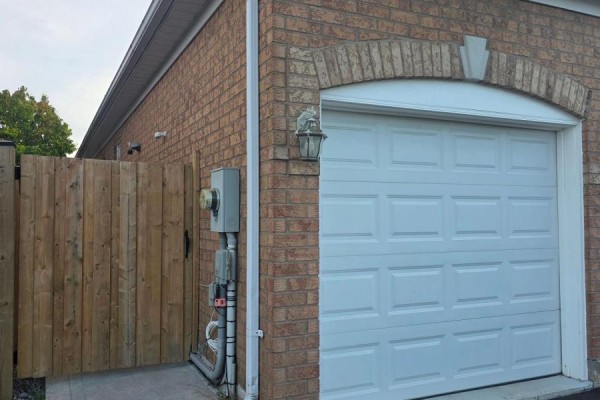 White double garage door with brick facade and a wooden fence on the side. - Bsmt - 1022 Glenbourne Drive, Oshawa