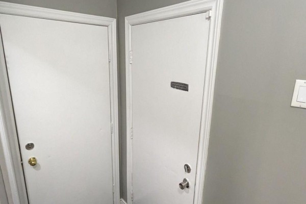 Interior hallway with two white doors, one with a metal label, against a grey wall. - Bsmt - 104 Randall Avenue, Markham