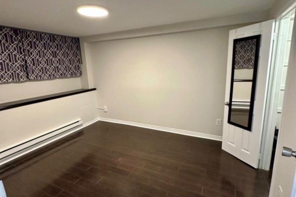 Bedroom with dark wood floors, grey walls, a white radiator, and a patterned curtain. - Bsmt - 13 Sorauren Avenue, Toronto