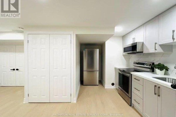 A basement kitchen with light grey and white cabinets, stainless steel appliances, a refrigerator, and double doors. - Bsmt - 1443 Cooper Court, Oakville
