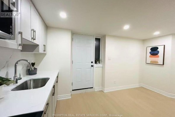 A basement kitchen with white cabinets, stainless steel sink, white countertops, and a white door with a window. - Bsmt - 1443 Cooper Court, Oakville