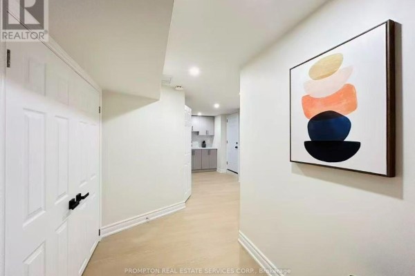 A hallway with white doors, light wood flooring, and a colorful abstract art piece on the wall. - Bsmt - 1443 Cooper Court, Oakville