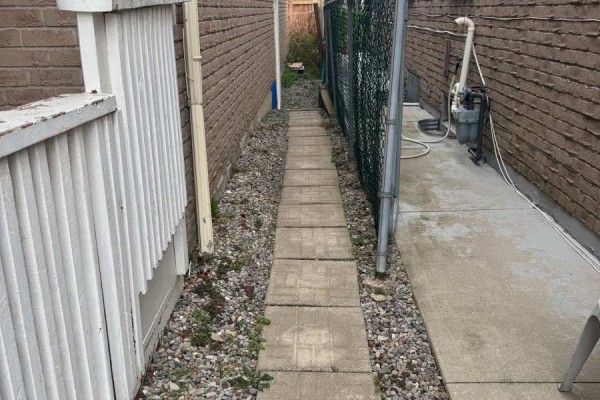 Narrow side yard with stone path, gravel, fence, and utility equipment. - Bsmt - 147 Morton Way, Brampton