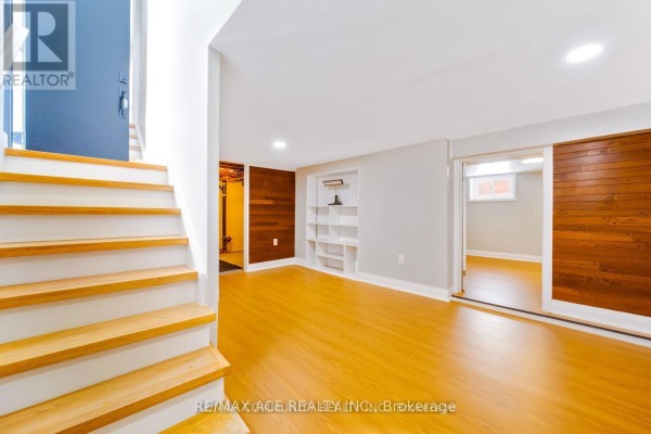 Basement living area with light wood laminate flooring and built-in white shelving. - Bsmt - 15 Cree Avenue, Toronto