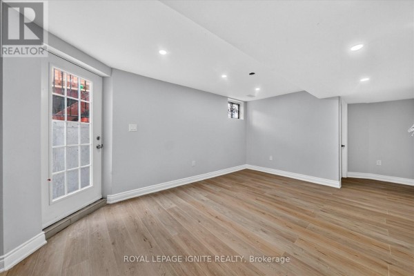 Basement room with light grey walls, wood-look flooring, and a glass door. - Bsmt - 15 Starry Crescent, Toronto