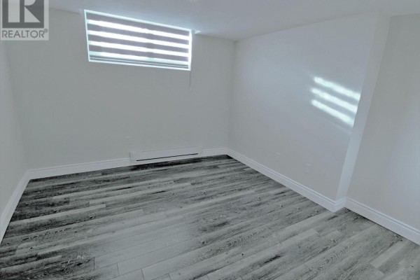 Empty room in basement with wood-look flooring, window with blinds, and heating unit. - Bsmt - 158 Coxwell Avenue, Toronto
