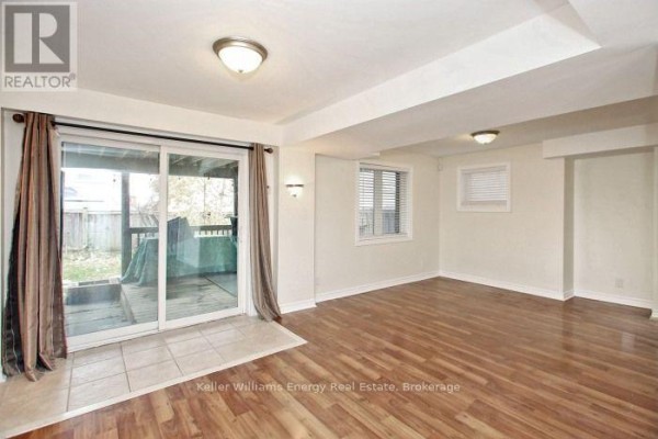 Basement living area with wood laminate flooring, featuring a sliding glass door to the backyard. - Bsmt - 1646 Quail Run Drive, Oshawa