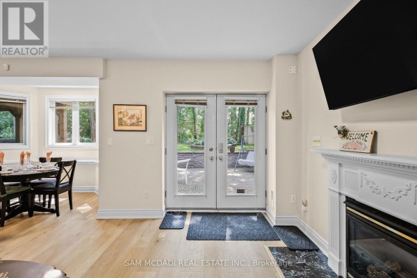 Living area with a gas fireplace, television, dining table with chairs, and double glass doors leading outdoors. - Bsmt - 1770 Fellen Place, Mississauga
