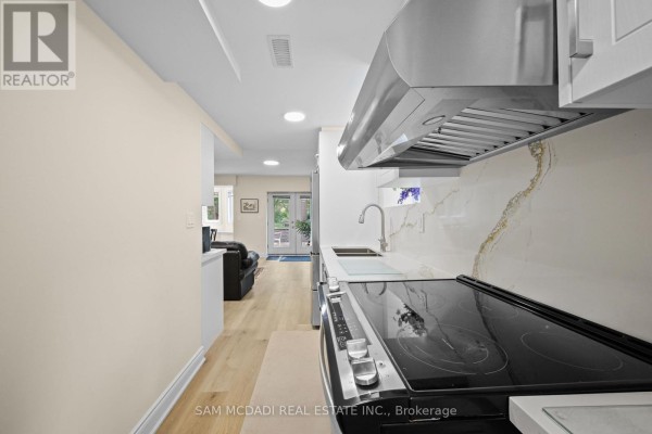 View down a basement hallway showing a small kitchen with white cabinets and a living area with double doors. - Bsmt - 1770 Fellen Place, Mississauga