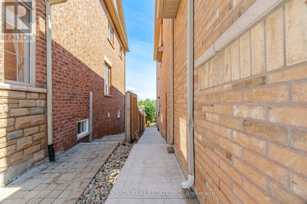 Narrow walkway between brick houses with patterned pavers and a concrete path. - Bsmt - 18 Intrigue Trail, Brampton