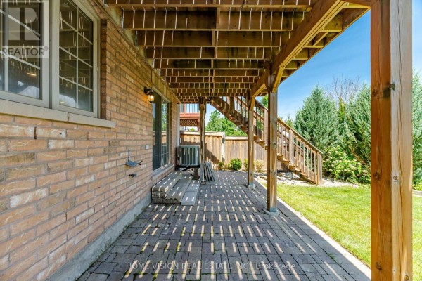 Covered patio area with brick flooring under a wooden deck with wooden stairs. - Bsmt - 18 Intrigue Trail, Brampton