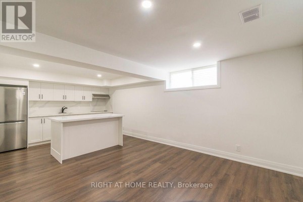 Basement with white kitchen, island, stainless steel fridge, and wood floors. - Bsmt - 186 Driscoll Road, Richmond Hill