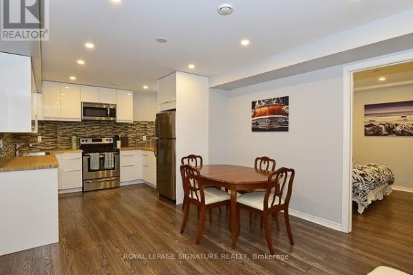 Basement living area with kitchenette, wooden dining table, and doorway to bedroom with bed. - Bsmt - 21 Melbert Road, Toronto