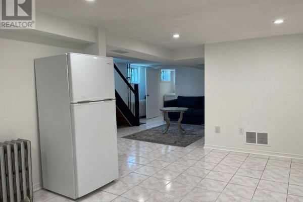 White refrigerator and tiled floor in a basement with a living area visible beyond. - Bsmt - 24 Weymouth Avenue, Toronto
