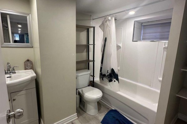 Basement bathroom with a sink, toilet, and a white bathtub with a shower curtain. - Bsmt - 25 Barnesdale Avenue S, Hamilton