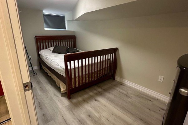 Basement bedroom with a dark wood crib-style bed, white bedding, and light wood flooring. - Bsmt - 25 Barnesdale Avenue S, Hamilton