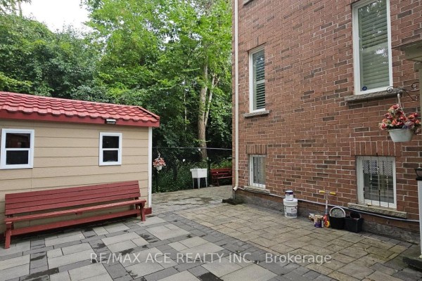 Rear exterior view showing the brick wall, windows, paved patio, and a garden shed. - Bsmt - 25 Fawnridge Trail, Toronto