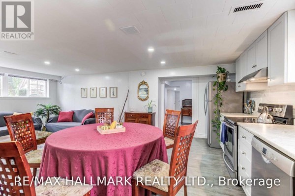 Basement open concept living and dining area with kitchen, dark grey sofas, and wooden table. - Bsmt - 30 Amarillo Drive, Toronto