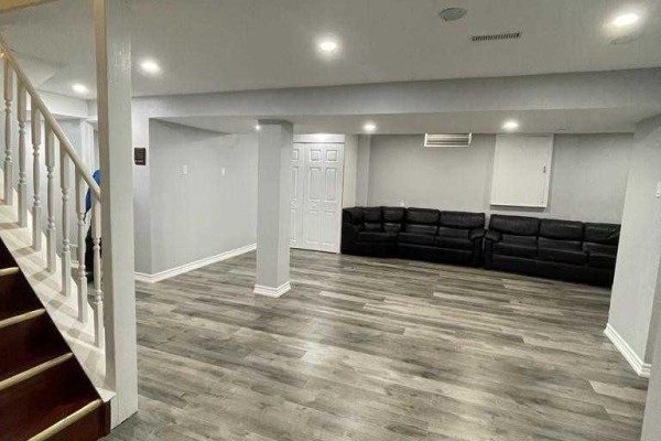 Finished basement living area with gray walls, laminate flooring, and black leather couches. - Bsmt - 304 Russet Way, Vaughan