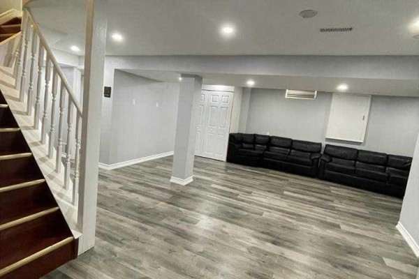 Finished basement living area with gray walls, laminate flooring, and black leather couches. - Bsmt - 304 Russet Way, Vaughan