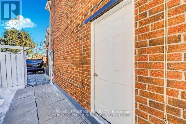 Exterior shot of a brick house side showing a white door and paved walkway with snow. - Bsmt - 32 Lansbury Drive, Toronto