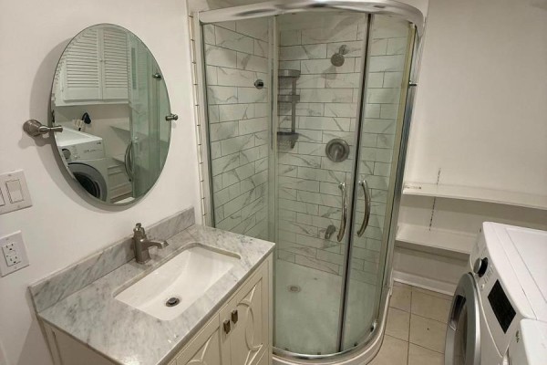A marble countertop vanity with a white sink is beside a glass-enclosed shower with white tile. - Bsmt - 4154 Sunflower Drive, Mississauga