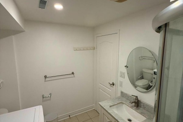 A white vanity with a marble countertop and sink is next to a shower and toilet in a bright room. - Bsmt - 4154 Sunflower Drive, Mississauga