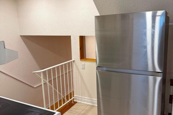 A stainless steel Samsung refrigerator stands next to a staircase with white railings and a small wooden window. - Bsmt - 4154 Sunflower Drive, Mississauga