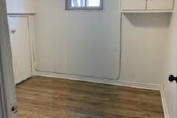 Empty basement living area with wood laminate flooring and white walls. - Bsmt - 49 Longford Drive, Newmarket