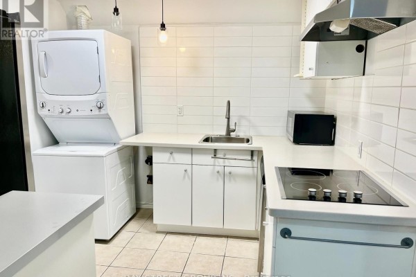 Basement kitchen with white tiled backsplash, white cabinets, and stacked washer and dryer. - Bsmt - 5 King William Crescent, Richmond Hill