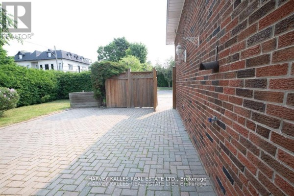 Side view of a brick house exterior with a paved driveway and wooden fence. - Bsmt - 550 Glencairn Avenue, Toronto