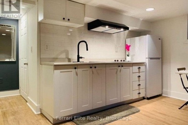 Closeup of a white basement kitchen with a black faucet, white subway tile backsplash, and stainless steel refrigerator. - Bsmt - 66 Richmond Street, Richmond Hill